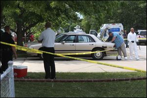 Police and investigators look through the trunk of a car outside 12313 Washington St.