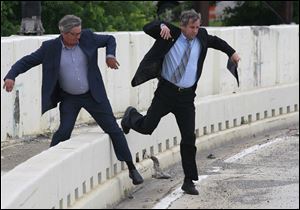 Lucas County commissioner Pete Gerkin, left, and Sen. Sherrod Brown hop over a highway barrier on their way to a press conference at the Anthony Wayne Bridge in Toledo.