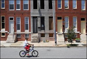 A youth rides a bicycle past a blighted property that will be restored by Come Home Baltimore. The run-down unit is sandwiched between renovated properties on North Bond Street in Baltimore’s Oliver neighborhood.