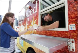 Laura Ness is served by John Ray from The Displaced Chef food truck on St. Clair Street downtown. The pilot program for food trucks in Toledo began last year at the request of then-Mayor Mike Bell.