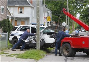City workers try to remove a Toledo Police Department vehicle from the yard of a home on East Broadway after an early morning crash.