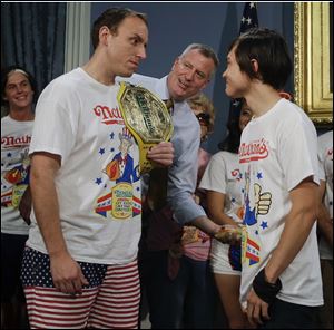 New York City Mayor Bill de Blasio watches Joey Chestnut, left, and Matt Stonie, right, during a news conference to promote the upcoming Nathan's Famous Fourth of July Hot-Dog Eating Contest at City Hall in New York.