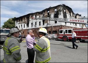Fire officials observe the scene of a burned three-story apartment and business building in Lowell, Mass., today, where officials said seven people died in a fast-moving pre-dawn fire. 