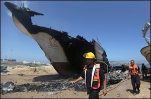 Palestinian firefighters walk around a boat hit in a missile strike at the port Friday in Gaza City.