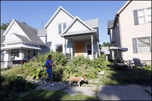 Robert Sims walks past 44 Garfield Place in East Toledo with his dog Papa. Neighborhood residents began complaining about the high grass there in May, 2013. The city of Toledo finally cut the grass last week.