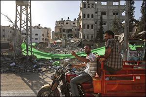 Palestinians drive past a building destroyed by an Israeli strike.