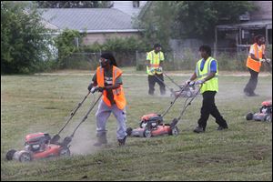 pathways16p Supervisor Willie Martin, left, leads a group of young men, members of the Pathway's summer employment program, as they work together mow a lot on Bakewell Street in East Toledo. 