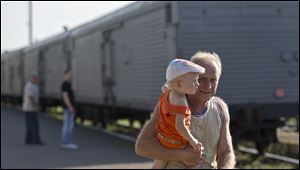 A man holds a baby as he walks next to a refrigerated train loaded with the bodies of victims in Torez, eastern Ukraine, nine miles from  the crash site of Malaysia Airlines Flight 17 on Sunda. Armed rebels forced emergency workers to hand over all 196 bodies recovered from the Malaysia Airlines crash site and had them loaded Sunday onto refrigerated train cars bound for a rebel-held city, Ukrainian officials and monitors said.