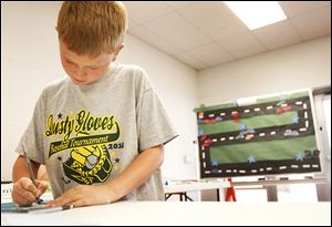Fourth-grader Collin Berryman, 9, writes his name on a slip of paper to enter into a drawing for a grand prize during the summer math club at Coy.