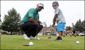 PGA pro Milton Carswell, Jr., helps Michael Rosales, 4, sink a putt during the ‘‍Mornings with Milton’ children’s summer golf camp at Collins Park Golf Course in East Toledo.