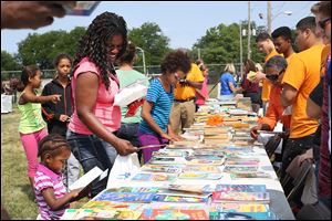 Cynthia Carter, center left, smiles as her daughter Malayiah, 2, picks out a book during a cookout and book giveaway put on Tuesday by the organization Books 4 Buddies and Toledo Public Schools near the LMHAS's Weiler Homes in East Toledo.