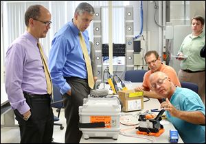  Thomas Perez, left, and Arne Duncan  watch as journeyman electrician Randy Artman of Hudson, Mich., right, demonstrates the process for splicing high-speed fiber optic cable.
