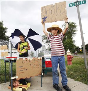 Courtney Hall, 8, left, rests under the table as Zach Hall, 13, right, and Jacob Hall, 11, look for customers on Thursday at their drink stand.