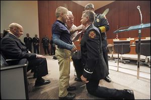Christopher Burns, who was promoted from lieutenant to captain in the Toledo Fire Department, is pinned by his son, Aiden Burns, 9, left, and his father, Ed Burns, center.