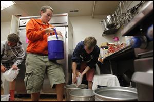 Tynan Hubbell, 14, left, a Saint Johns High School sophomore, Aidan Hubbell, 19, center, a BGSU sophomore, and Peter Funk, 20, right, a BGSU sophomore work to pour out water from various containers at the Martin Luther King Center Kitchen for the Poor.