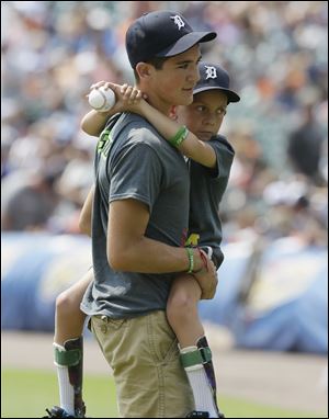 Braden Gandee, 7, held by his brother Hunter is seen after tossing out the ceremonial first pitch before an interleague baseball game between the Detroit Tigers and the Colorado Rockies on Sunday in Detroit.
