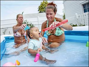Myah Brown, center, 11 months, celebrates the end of bottled-water baths with Connie Elter, left, and Dawn Szych, Myah’s grandmother, at Ms. Szych’s West Toledo home. Many say they might bathe in the water, but they won’t drink it. 