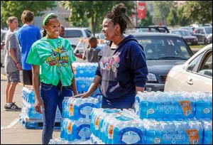 Volunteers Dakari Parish, left, 13, and Ayanna Bishop, right, 17, hand out free water in the receiving area at Central Catholic on Monday despite the all-clear declaration issued by Mayor Collins and other officials.
