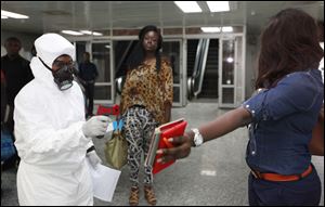A passenger holds personal possessions as a Nigerian port health official uses a thermometer on her at the arrivals hall of Murtala Muhammed International Airport in Lagos, Nigeria.
