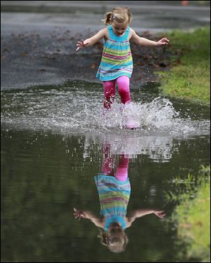 Lucy Baechle, 3, plays in the flooded street of Brookford Drive in Toledo after one of Monday’s torrential downpours.