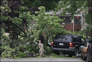 Frank McKinney moves branches from a large downed tree branch that fell across Vasser Street so his wife, Lisa, can pull into the driveway of their Toledo home.  The tree is blocking the entire street.