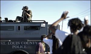 A member of the St. Louis County Police Department points his weapon in the direction of a group of protesters in Ferguson.