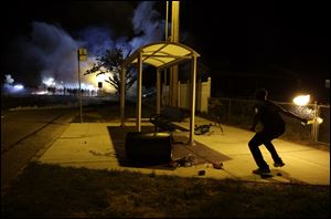 A man picks up a flaming bottle and prepares to throw it as a line of police advance in the distance.