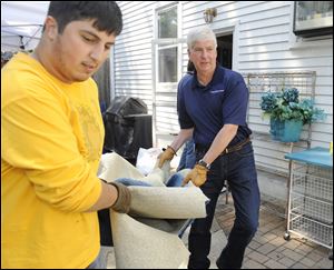 Michigan Gov. Rick Snyder, right, and  volunteer  Ali Emamdjomeh, remove damaged carpet Friday from the basement of the home of Matthew and Kathy Cahaney in Royal Oak, Mich.
