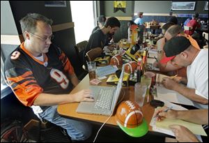 Brian Sherman, left, uses his laptop to record moves in his team's fantasy football draft. Many Americans spend work hours reviewing player statistics and managing their pretend rosters.