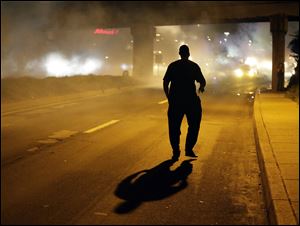 A man walks in the street after police fired tear gas to disperse a crowd Sunday during a protest for Michael Brown, who was killed by a police officer last Saturday in Ferguson, Mo.