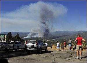 A fire creates a plume of smoke watched by onlookers along Highway 41 south of Oakhurst, Calif., Monday.
