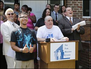Paul Vagts speaks at the podium outside his Cherry Street home as his stepson, Kyle Hammond, gives a thumbs up. Behind them are Michael Marsh from the Toledo Fair Housing Center, left, and Wade Kapszukiewicz, chairman of the Lucas County Land Bank. 