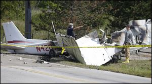 Investigators look over the wreckage of a plane crash as it rests on the side of a road.
