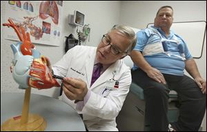 Dr. Michael Moront uses a model of a heart to explain Rick Sobecki's recent valve replacement surgery to Mr. Sobecki, right, at ProMedica Toledo Hospital.