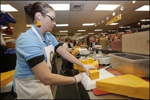 Karen McConaghie, decked out in cheese-shaped earrings, cuts blocks of cheese for customers at The Andersons.