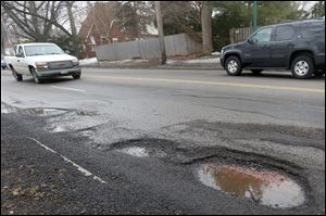 Cars pass near splattered asphalt and a deep pothole in Toledo