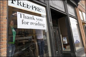 Toledo Free Press employees Christie Materni, left, and James A. Molnar hang up a good-bye sign in the window of the newspaper’s offices.
