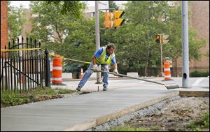 Eddie Garcia, a worker with Toledo’s Division of Streets, Bridges, and Harbor, levels the concrete sidewalk and curb installed as part of repairs along North Superior Street near Cherry Street.