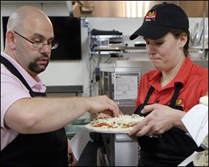 Trainer Chuck Blevins of Lincoln Park, Mich., spreads cheese on a pizza held by Sara Ragsdale of Charleston, S.C., in Marco’s new test kitchen on Monroe Street. Marco’s was named the second-fastest growing chain in the nation.