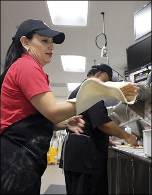 Delmy Lopez of Smyrna, Ga., stretches dough for a medium-sized pizza. Behind her, Ed Alimi of San Diego, applies sauce to a crust.