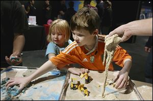 ‘This is weird and fun!’ Cora, 5, left, said as she and her brother Riley Puck, 9, played in a cement-like mix at a table run by the construction supply firm Chas E. Phipps Company at the Imagination Station. 