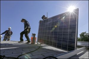 Workers install solar panels on a roof in Los Angeles in February 2016. A vote on a proposed solar array at Overland Industrial Park in Toledo was dropped from city council’s agenda this week.