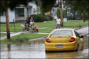 Pedestrians watch as a car is stuck attempting to drive through water on Sandusky Street on Thursday in Findlay.