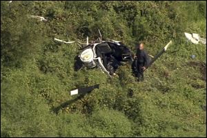 In this image from video provided by NBC10 Philadelphia, a first responder examines the wreckage of a helicopter in Lumberton, N.J., Friday, Sept. 8, 2017. The official website for Montgomery Gentry says Troy Gentry, half of the country duo, died in the crash.