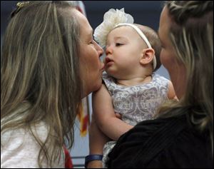 Margot Joyner, 8 months, center, who is being adopted, gets a kiss from her grandmother Janet Barnhill, left, while being held by her adoptive mother Nikki Joyner, right, of Swanton, during a public adoption ceremony at Lucas County Children Services to honor 