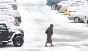 A pedestrian makes her way across a snow-covered parking lot on Orange Street Monday, March 13, 2017, in downtown Toledo.  