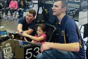 Addison Hendricks, 6, of Oregon, center, racing in a car made by UT students for the Formula SAE competition. With her are University of Toledo students Michael Gordon, of Harrisburg, Pa., left, and Ben Wolak, of South Lyon, Michigan.
