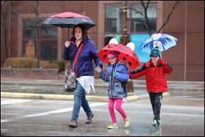 Nicole Sobieski and her children, Rhiannon, 8, and Jacob, 6, of Allen Park, Mich., dodge raindrops and puddles as they cross Summit Street en-route to the Imagination Station Monday, February 19, in Toledo.