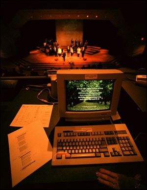 A computer displays lyrics that are projected onto a screen on the stage at Wetgate Chapel.