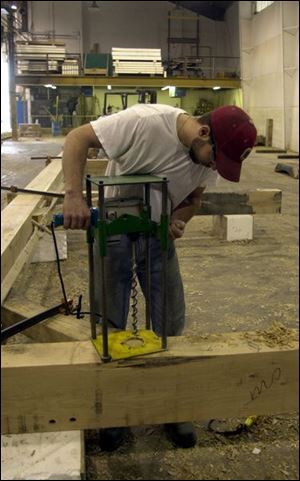 Travis Binion drills pin holes in a piece of timber at Riverbend Timber Framing and Insulspan. The companies craft timber frames and insulated panels.